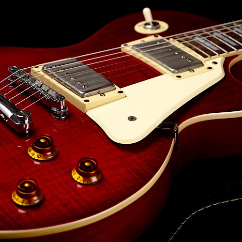 The image shows a close-up of a red electric guitar with a glossy finish, highlighting its strings, pickups, and four control knobs on the body.