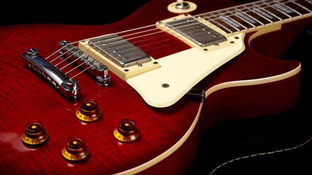 The image shows a close-up of a red electric guitar with a glossy finish, highlighting its strings, pickups, and four control knobs on the body.