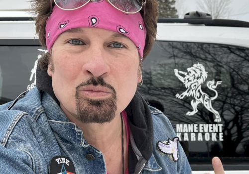 A person in a pink bandana with sunglasses poses in front of a vehicle with a logo that says "MAIN EVENT KARAOKE."