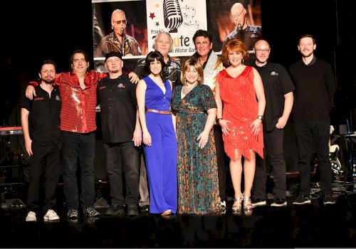 A group of people standing on a stage, with a backdrop featuring microphones and performers, wearing a variety of outfits.