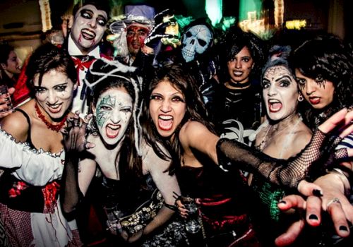 The image shows a group of people in Halloween costumes and makeup, posing and making expressive faces.