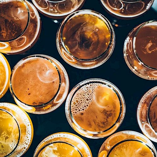 The image shows an overhead view of various glasses filled with different types of beer, displaying a range of amber and golden hues.