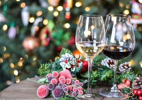 Two glasses of wine, one white and one red, are on a table with festive decorations and a blurred Christmas tree in the background.