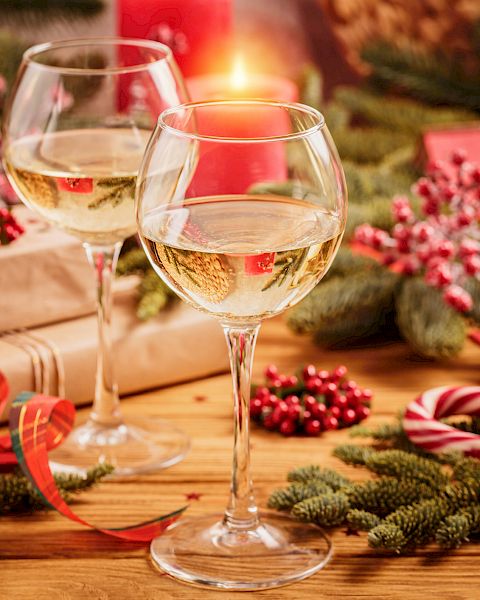 Two wine glasses, wrapped gifts, and festive decorations, including pine branches, berries, a candy cane, and ribbon.