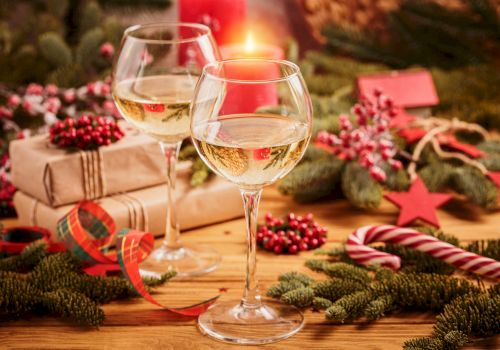 Two wine glasses, wrapped gifts, and festive decorations, including pine branches, berries, a candy cane, and ribbon.