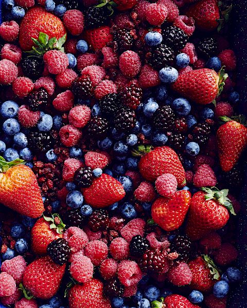 The image contains an assortment of fresh berries, including strawberries, raspberries, blueberries, and blackberries, all mixed together.