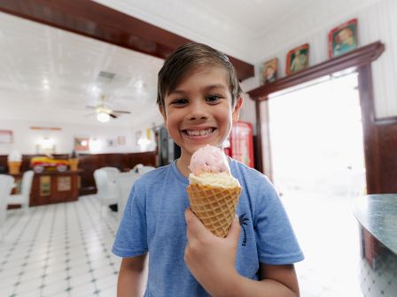 A boy in a blue shirt is smiling while holding an ice cream cone in what appears to be an ice cream parlor.