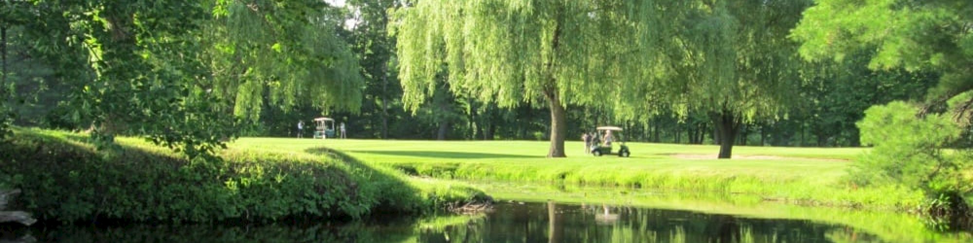 The image shows a tranquil pond surrounded by lush green trees and a grassy area, with golf carts in the background, reflecting a serene landscape.