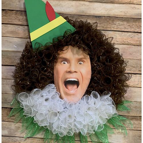 A humorous wreath featuring a person's face with a curly wig, elf hat, and mesh ruffle collar on a wooden background.