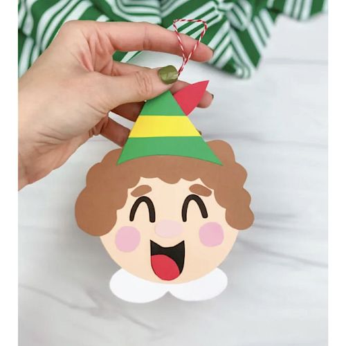 A hand is holding a festive ornament shaped like a smiling face with a party hat.